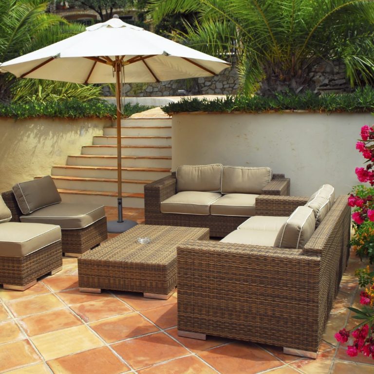Outdoor seating area with cushioned furniture and a large umbrella, surrounded by greenery.